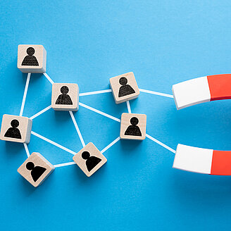 Fachkräftesicherung – © AndreyPopov / iStock.com Das Foto zeigt zwei Hände, die einen Magneten halten, der kleine Plättchen mit menschlichen Silhoutten anzieht.